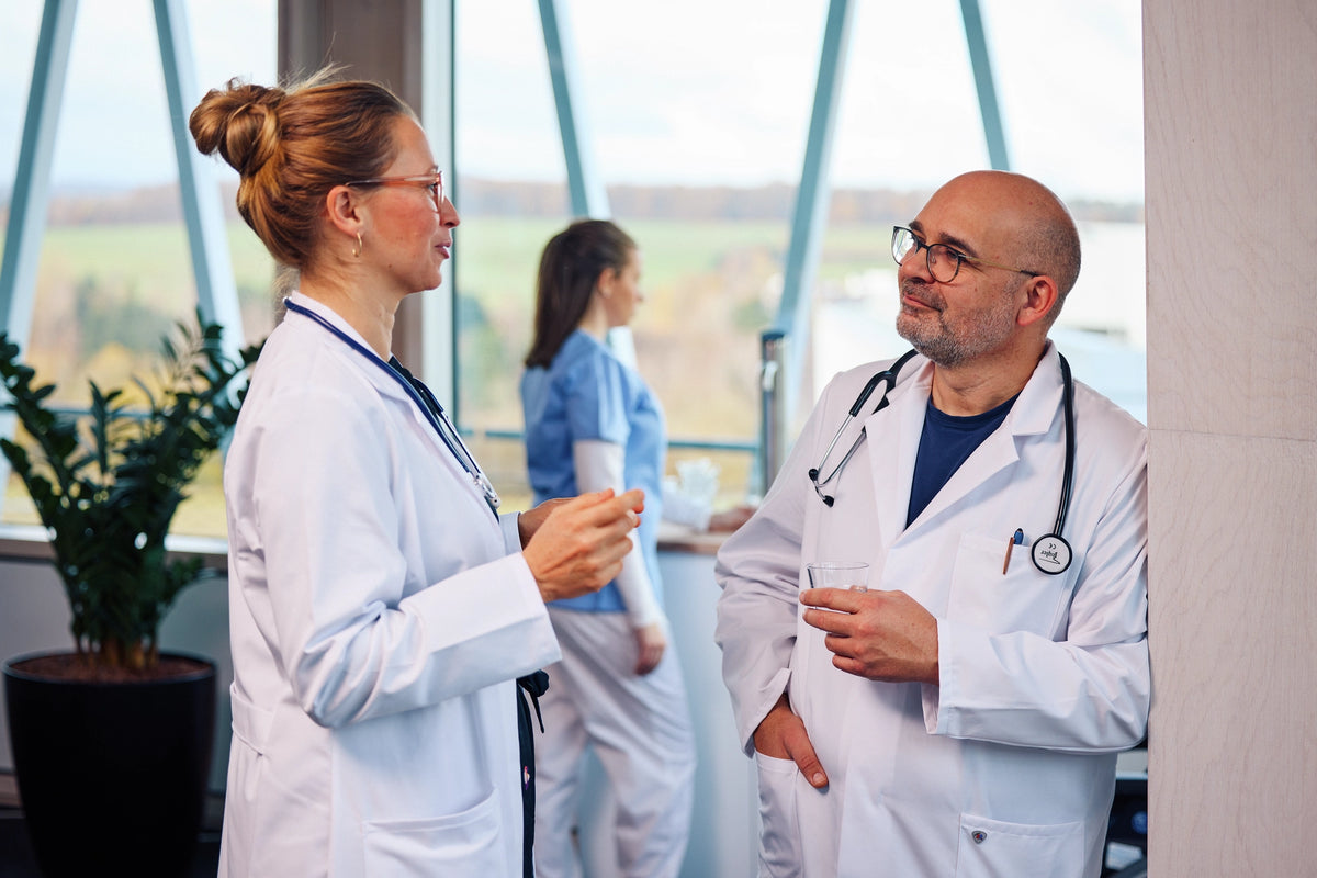 Two doctors in a conversation in a hospital setting, with a person in the background